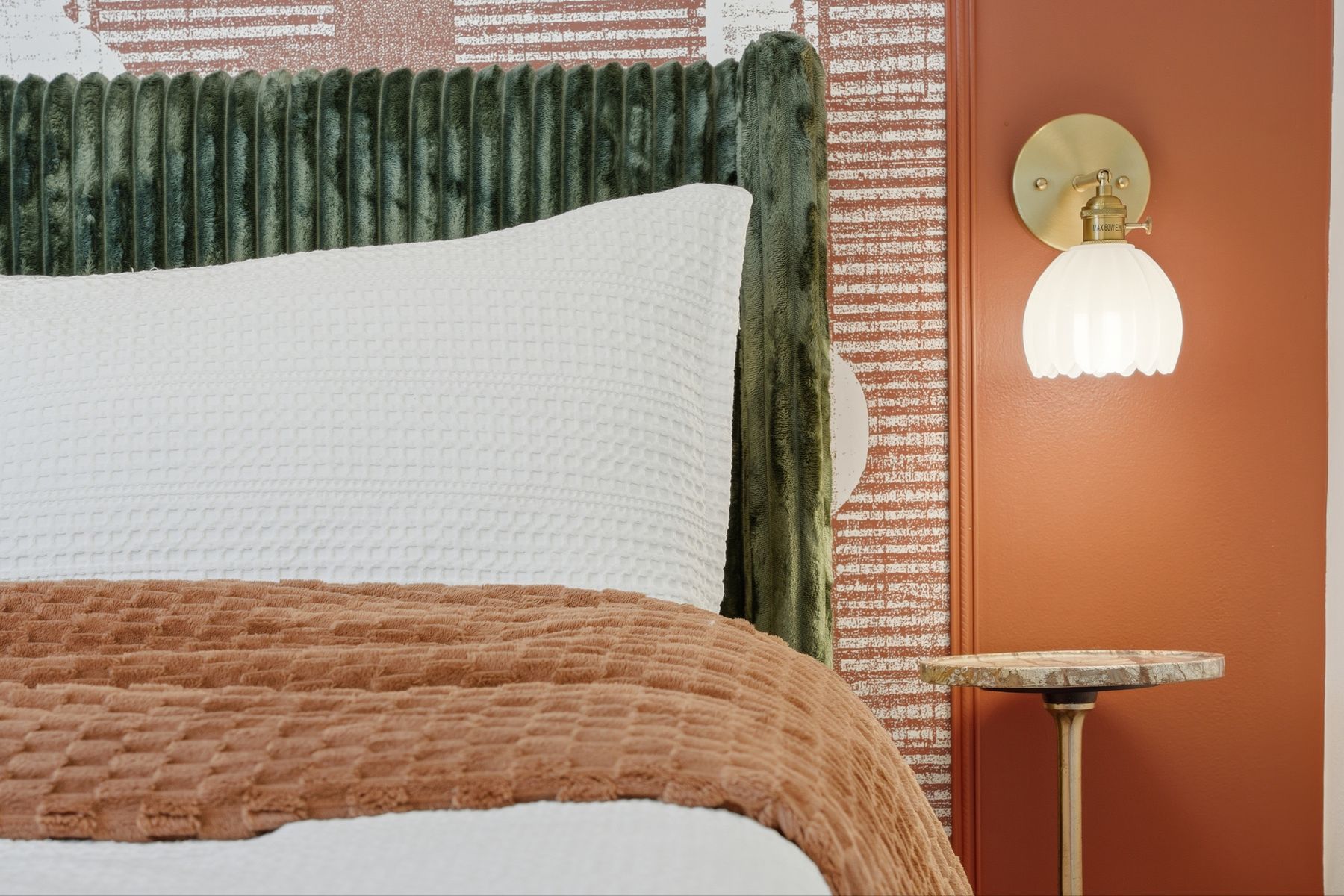 Green velvet headboard and a wall sconce