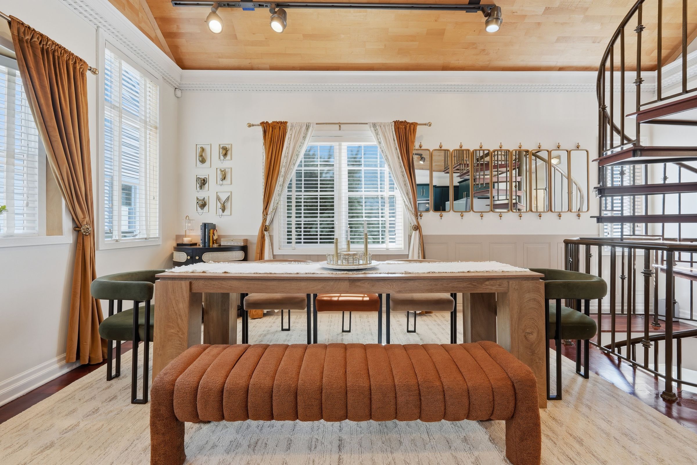 Dining room with a long table and bench, brass mirrors and a spiral staircase