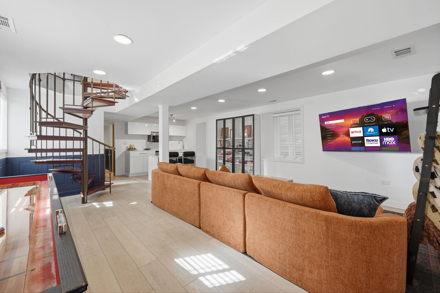 Lower-level lounge with a sectional, a spiral staircase and a shuffleboard table